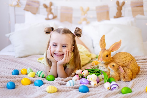 Easter a little girl with painted colored eggs tulips and a rabbit at home in a bright room is preparing for the holiday smiling and having fun