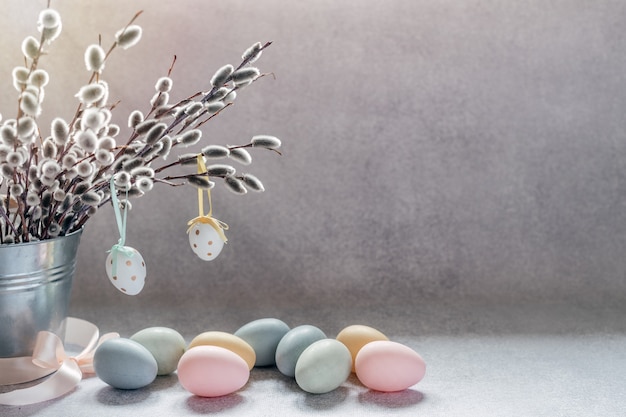 Минималистичный пасхальный фон с ветвями ивовой сережки в декоративном ведре и красочными пасхальными яйцами с копией пространства