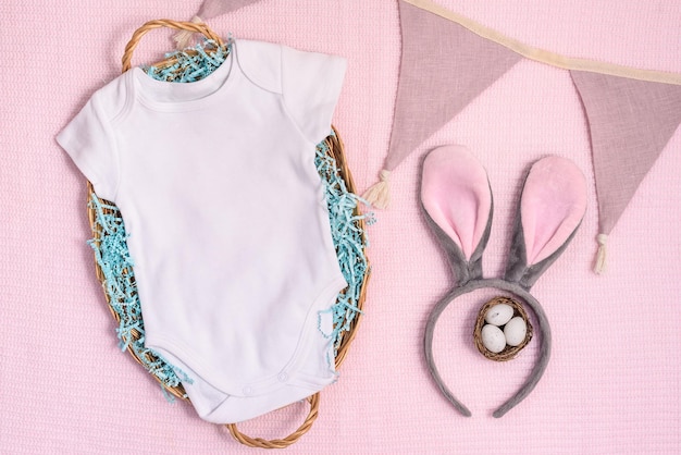 Easter mockup baby bodysuit with bunny and easter eggs on pink cover background flat lay copyspace