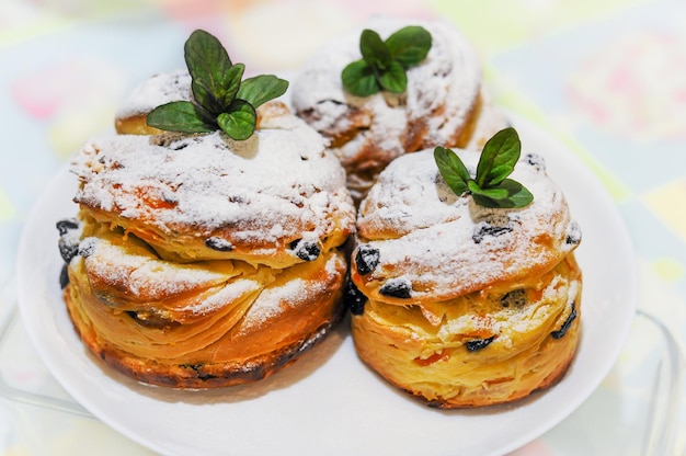 Пасхальные кексы craffin в белой сахарной пудре изюмом и листьями мяты на белой тарелке