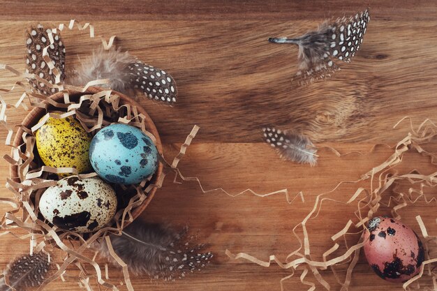 Easter nest made of hay with painted colored eggs and feathers on a wooden background. Flat flat, top view, copy space. Easter background. Easter concept in a traditional retro style.