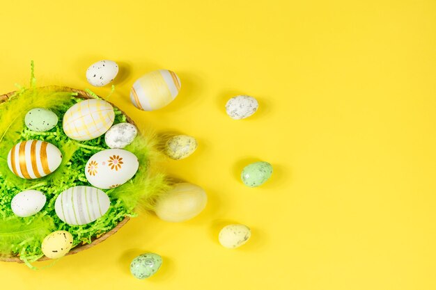 Easter nest with eggs and feathers on a yellow background view from above place for text