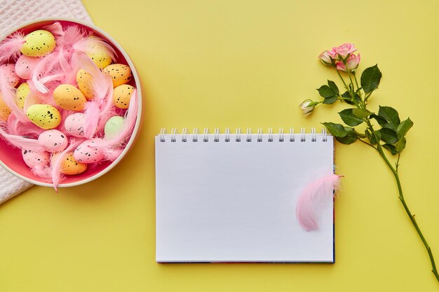 Easter notepad mock up Pink bowl with colorful eggs pink feathers and pink rose Happy Easter concept Post card mock up on yellow background