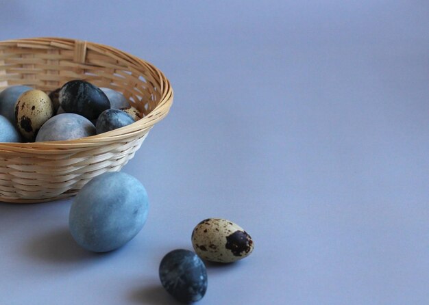 Easter painted blue and blue eggs in a straw cup and scattered on a blue background