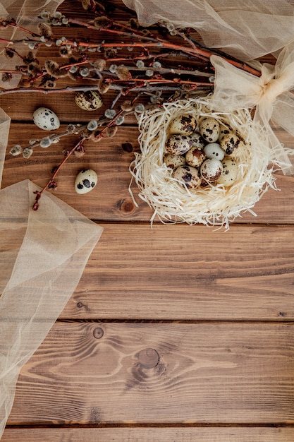 Easter quail eggs in nest and willow branch on a wooden background, copy space