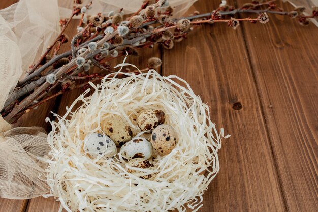 Photo easter quail eggs in nest and willow branch on a wooden background, copy space