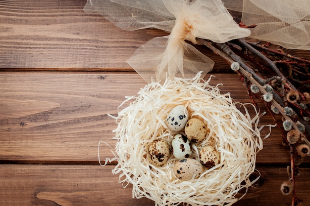 Пасхальные перепелиные яйца в гнезде и ветви ивы на деревянном фоне, копией пространства