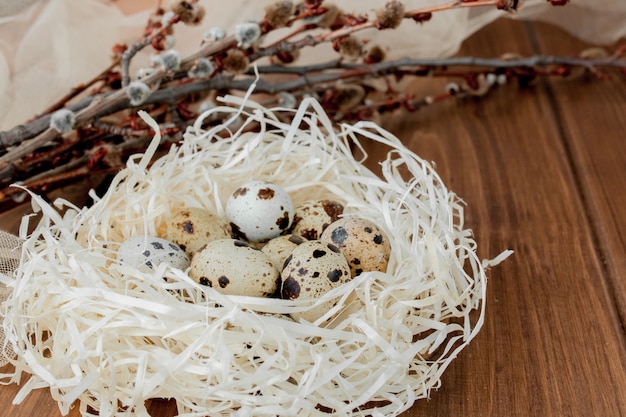 Пасхальные перепелиные яйца в гнезде и ветви ивы на деревянном фоне