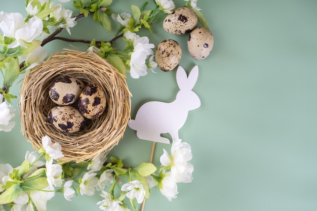 Easter quail eggs in straw nest and white easter bunny with blossoming branch