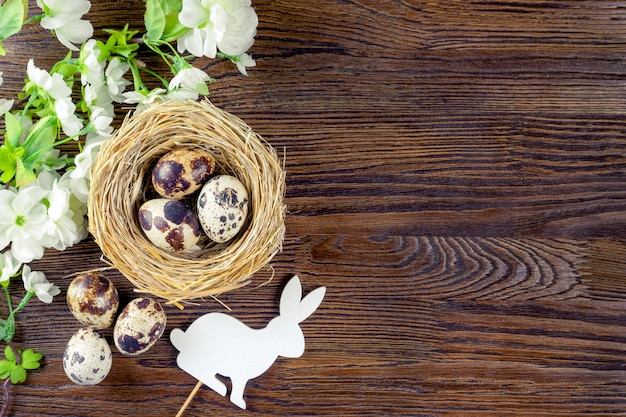 Uova di quaglia di Pasqua nel nido di paglia e coniglietto di Pasqua bianco con ramo in fiore