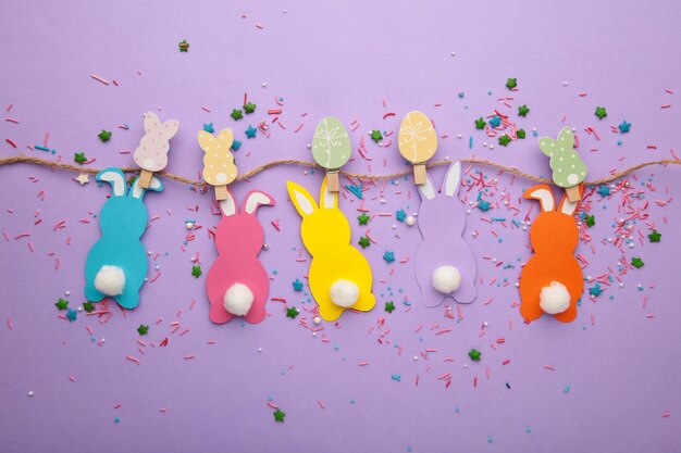 Easter rabbits handmade from colored paper on a rope with clothespins easy crafts for children on a purple background.