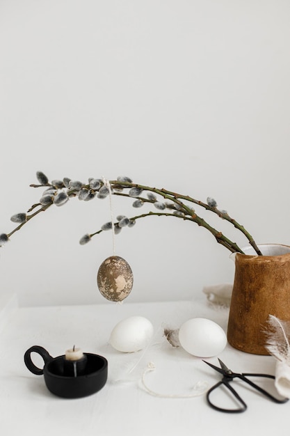 Foto pasqua natura morta rustica uova dipinte appese su rami di salice uova di piume di candela sul tavolo