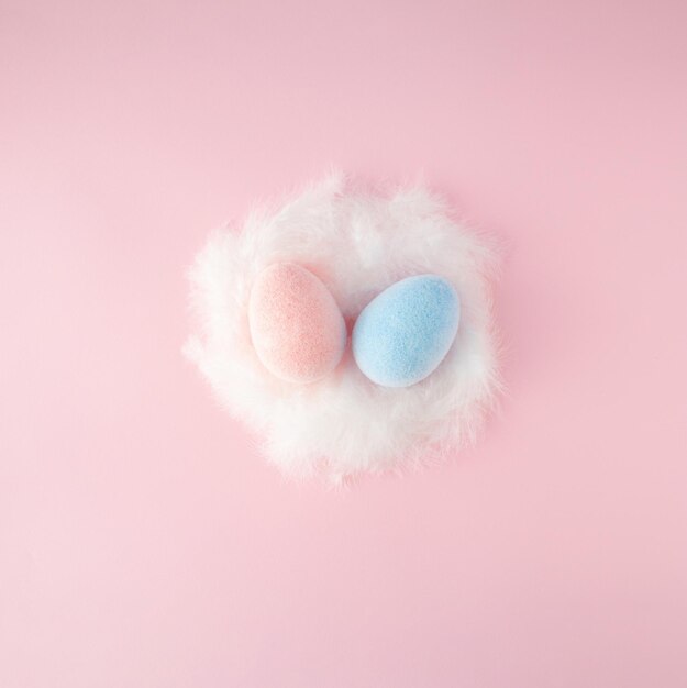 Easter scene with pink and blue egss in white feathered nest on pink background