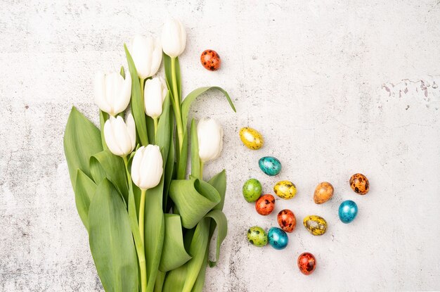 Easter and spring concept. Top view of white tulips and colored easter eggs on concrete backgrund with copy space