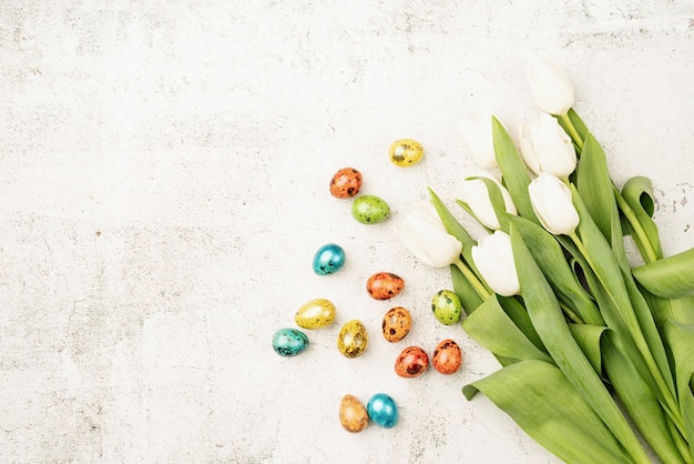 Easter and spring concept. Top view of white tulips and colored easter eggs on concrete backgrund