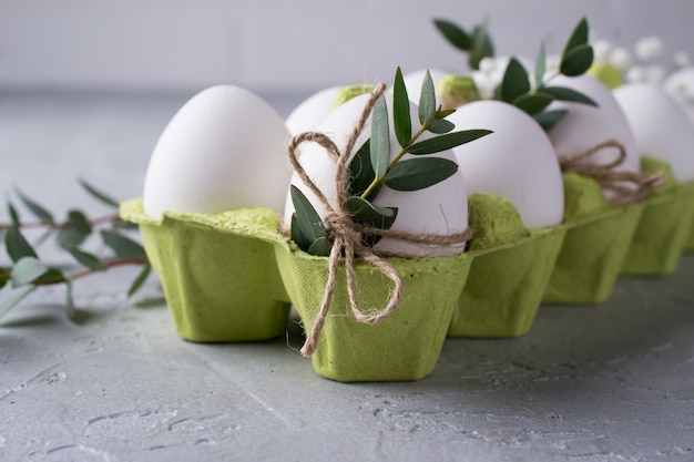 Easter spring decorative composition  with easter white chicken raw  eggs in green carton box Decorated with eucalyptus leaves