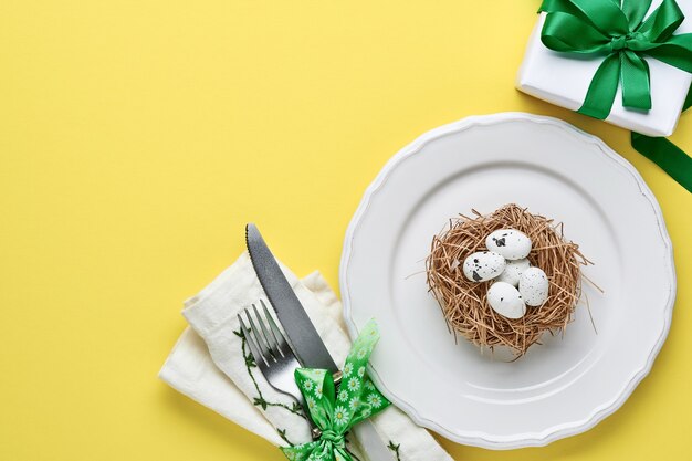 Regolazione della tabella di saluto di primavera di pasqua con confezione regalo con nastro verde, uova e carota dolce su sfondo di colore giallo tendenza. vista dall'alto. spazio per il testo.