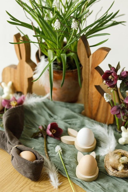 Easter still life Stylish wooden bunny spring flowers and natural eggs on rustic table in room Happy Easter Festive arrangement and decor in farmhouse