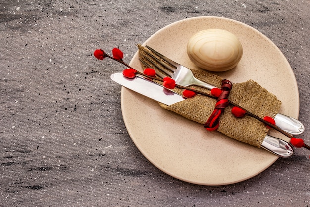 Easter table setting on gray concrete background. Spring holiday card template. Cutlery, egg, willow seals, vintage linen napkin