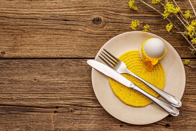 Easter table setting on old wooden background. Spring holiday card template. Cutlery, crochet napkin, egg, flowering sprigs of dogwood