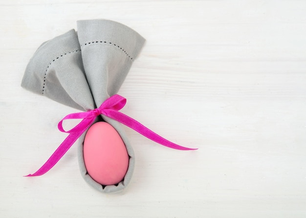 Easter table setting Pink Easter egg in a gray napkin rabbit ears shape on white wood