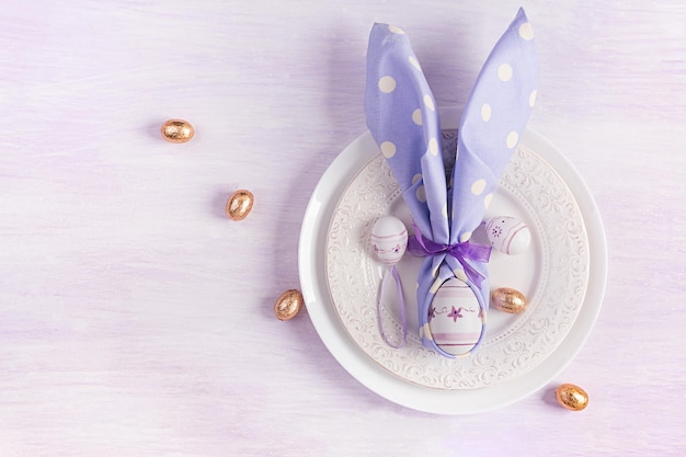 Пасхальный стол Белая тарелка с салфеткой, сложенной в форме кролика Пасха и шоколадные яйца на розовом фоне Счастливой Пасхальной праздничной концепции для кафе и ресторанов