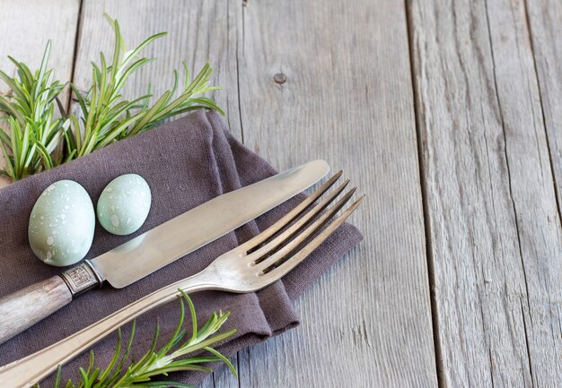 Easter table setting with eggs and rosemary on grey wooden table close up with copy space