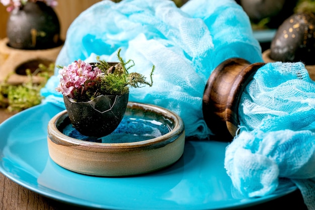 Easter table setting with empty turquoise ceramic plates decorated by forest moss black colored easter eggs and pink spring flowers on wooden table Stylish spring holidays Close up