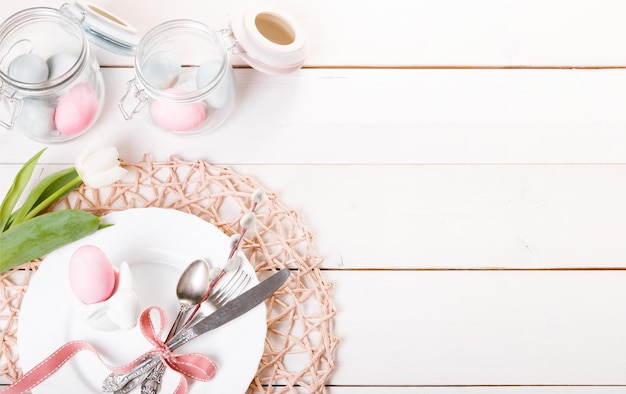 Easter table setting with pink and blue eggs and cutlery on white holidays background backdrop with