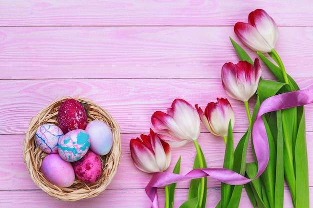 Easter theme with colorful eggs and  tulips over pink wood. Top view with copy space