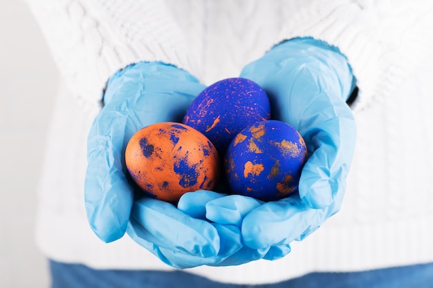 Easter time in quarantine concept. Female hands in blue medical gloves holding colored Easter eggs. Concept of Easter holyday and spring break during coronavirus