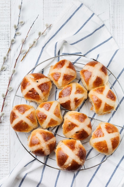 Easter traditional hot cross buns homemade on wooden tray with linen textile and willow branches on white wooden background. Selective focus. Top view. Copy space.