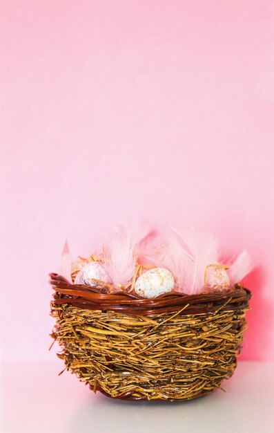 Photo easter vertical composition with traditional decor. small decorative colorful eggs in a wicker basket on pink background.