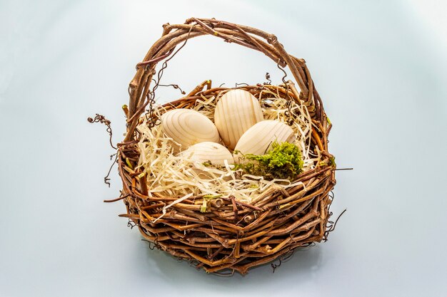 Photo easter wicker basket. zero waste, diy concept. wooden eggs, shavings, moss. light blue background