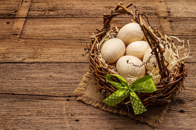 Easter wicker basket. Zero waste, DIY concept. Wooden eggs, shavings, satin bow. Old boards background