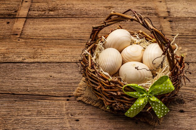 Easter wicker basket. Zero waste, DIY concept. Wooden eggs, shavings, satin bow. Old boards background