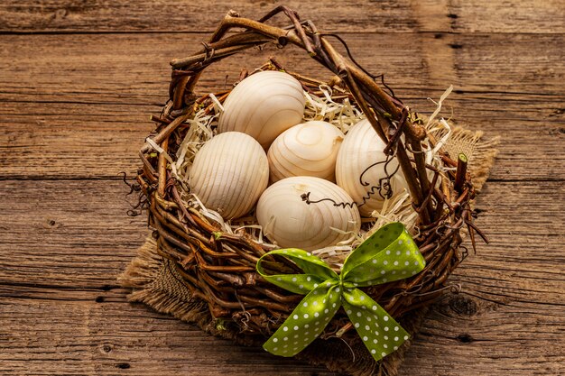 Easter wicker basket. Zero waste, DIY concept. Wooden eggs, shavings, satin bow. Old boards background