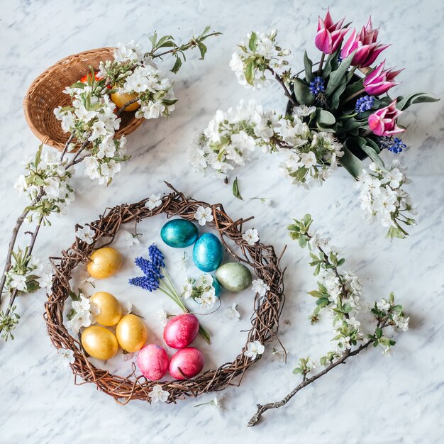 Easter wreath with dyed eggs and spring flowers and blossoming tree branches flat lay