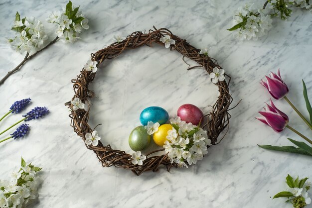 Easter wreath with dyed eggs and spring flowers and blossoming tree branches flatlay