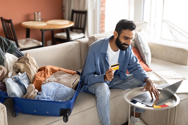 Eastern man using credit card and laptop booking trip indoor