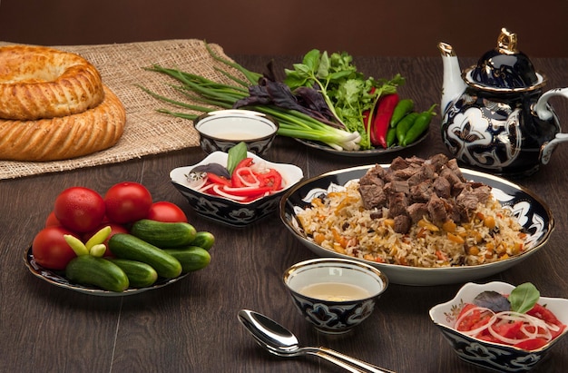 Eastern pilaf and salads with fresh vegetables, and cake and tea on a wooden board