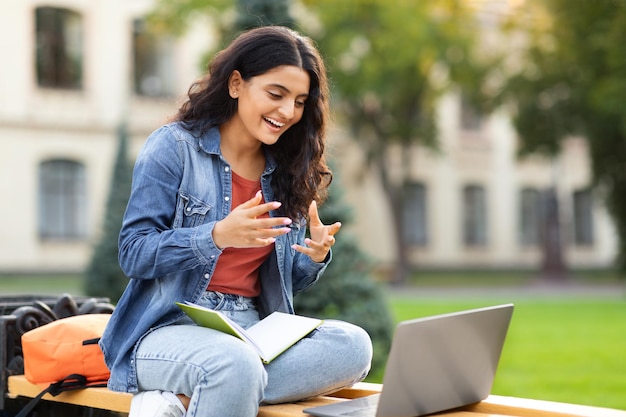 Молодая студентка с Востока сдает экзамен онлайн с помощью ноутбука на открытом воздухе.
