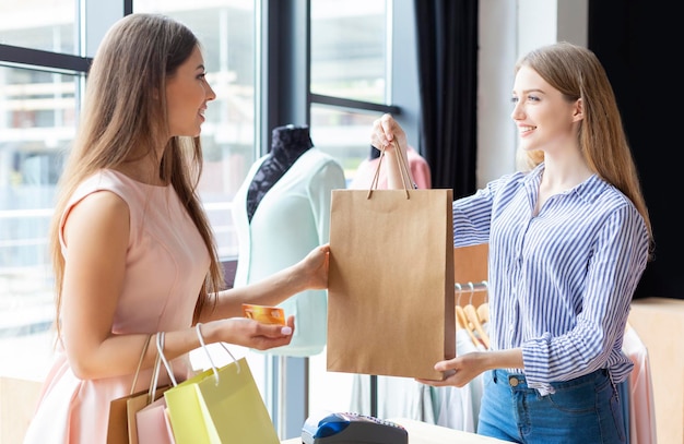 Foto acquisto facile. sorridente assistente femminile caucasica che dà acquisti al cliente presso lo showroom di abbigliamento