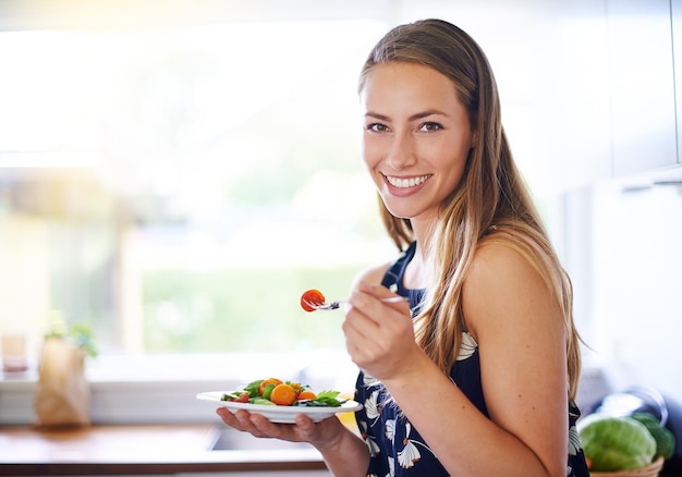 Eat healthy to live healthy Portrait of a young woman eating a bowl of strawberries at home