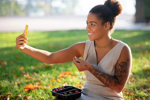 果実を食べる。公園で時間を費やして果実を食べながらselfieを作る晴れやかな女性