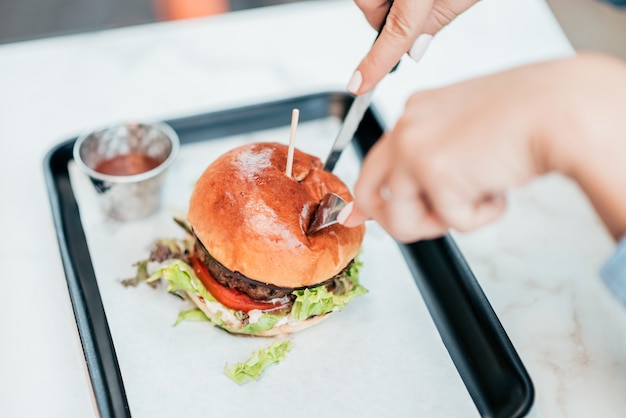 Eating burger with a fork and a knife.