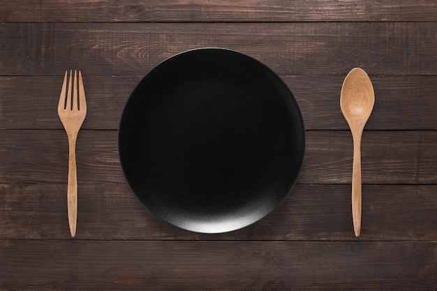 Eating concept. Spoon, fork and black dish on the wooden background