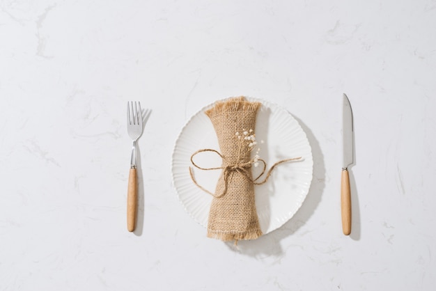 Mangiare il concetto. cucchiaio, forchetta e piatto bianco su sfondo di pietra bianca.