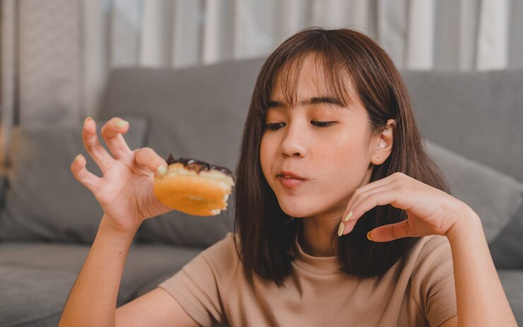 Photo 테이크아웃 및 배달 시 도넛을 먹습니다. 집으로 돌아가는 패스트푸드 테이크아웃. 거실에서 아시아 여성의 라이프 스타일입니다. 사회적 거리두기와 뉴노멀.
