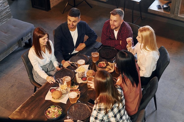 Mangiare e bere gruppo di giovani amici seduti insieme al bar con birra